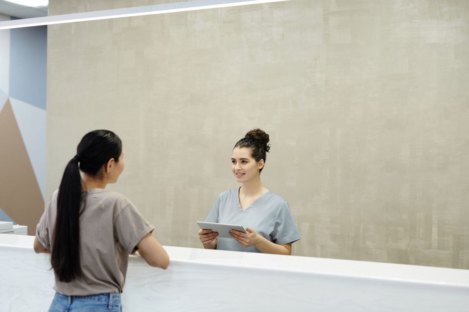 Recepcionista con tablet en una clínica moderna atendiendo a una paciente en el mostrador para agendar su cita