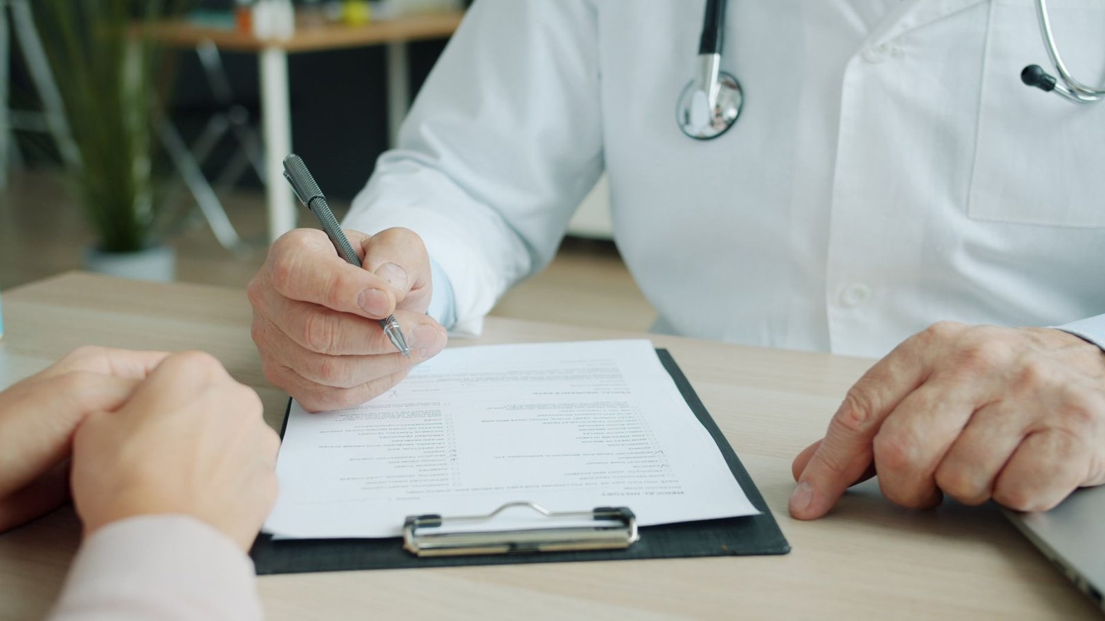 Primer plano de un médico con portapapeles explicando un documento a un paciente