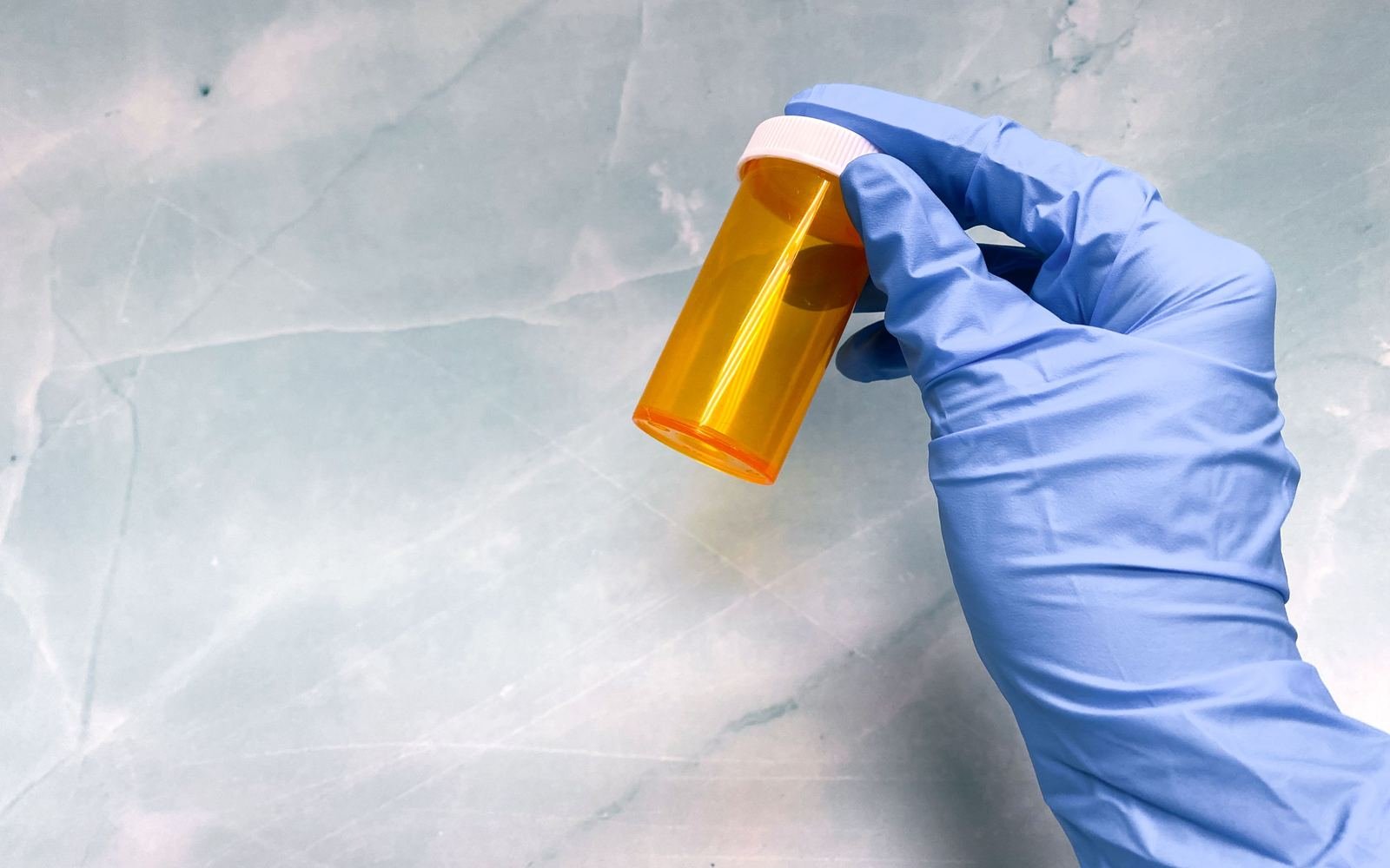 Mano con guante médico sosteniendo un frasco vacío de medicamento, sin rostro visible