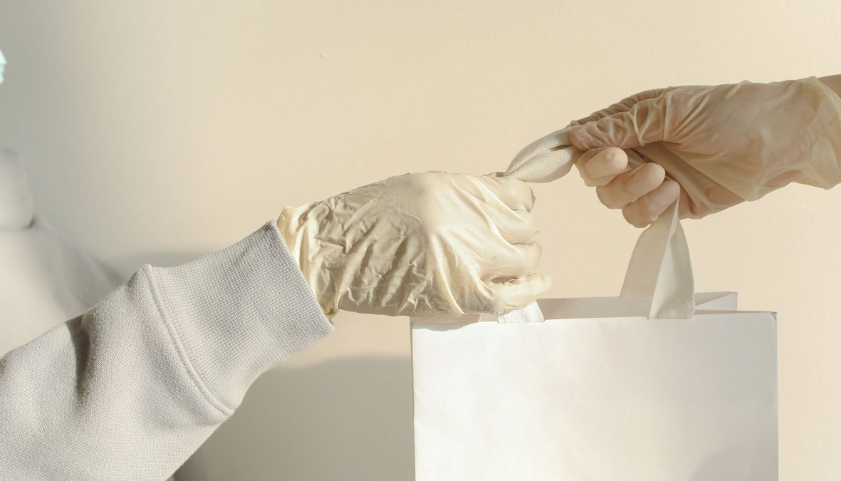 Manos con guantes entregando una bolsa discreta en el mostrador de una farmacia