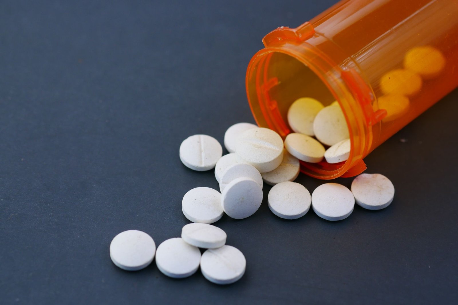Pastillas blancas derramándose de un frasco de medicamento anaranjado