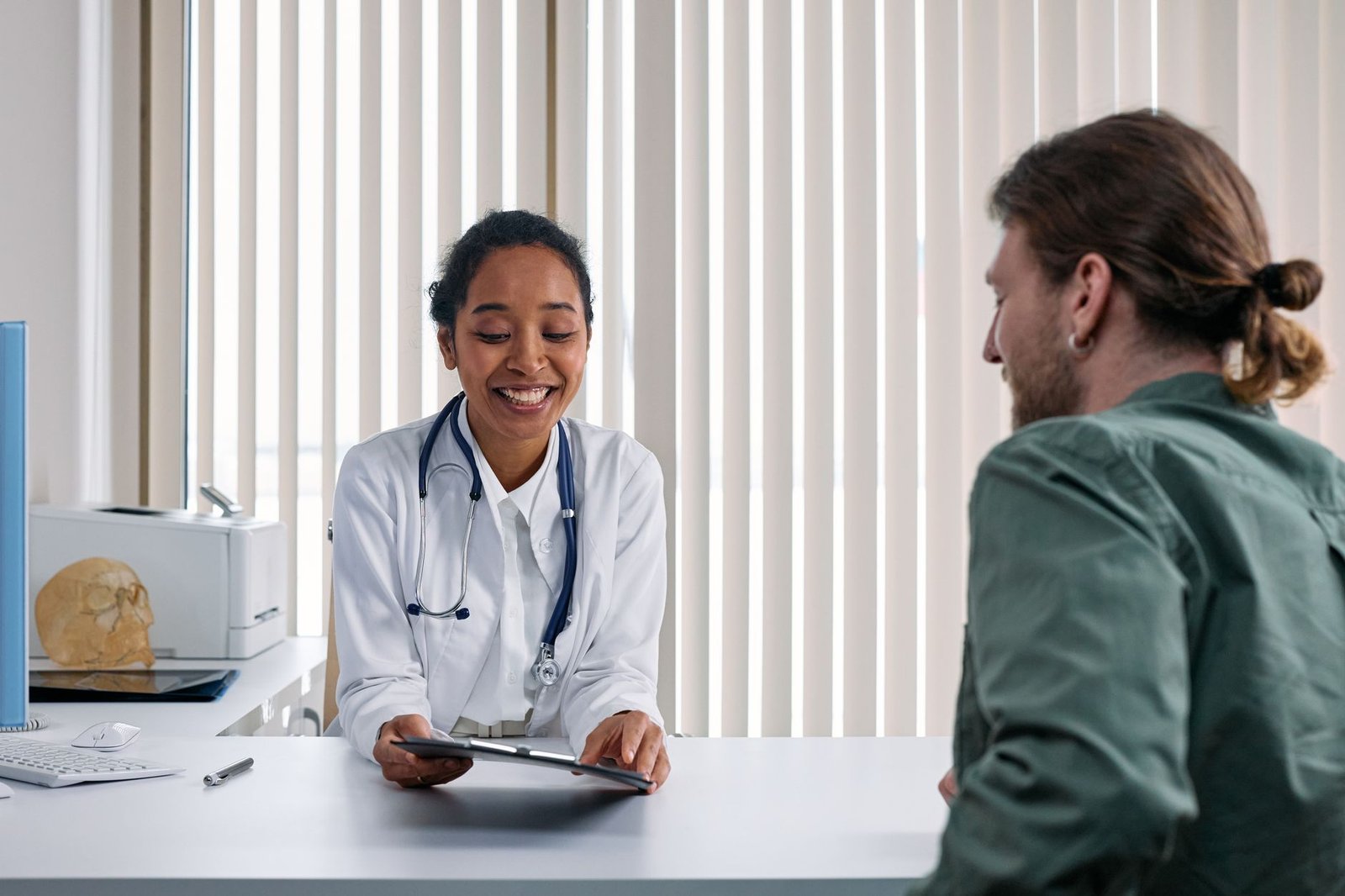 Profesional de la salud sonriente revisando información en una tableta durante una consulta médica con un paciente.