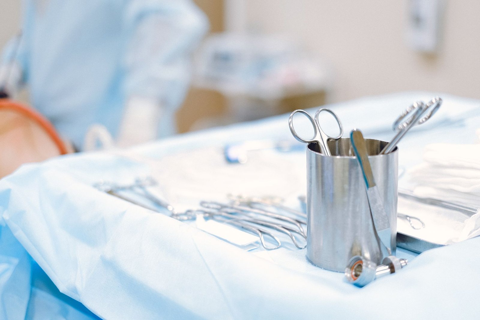 Instrumental quirúrgico esterilizado sobre una mesa clínica, con personal médico desenfocado y de espaldas al fondo