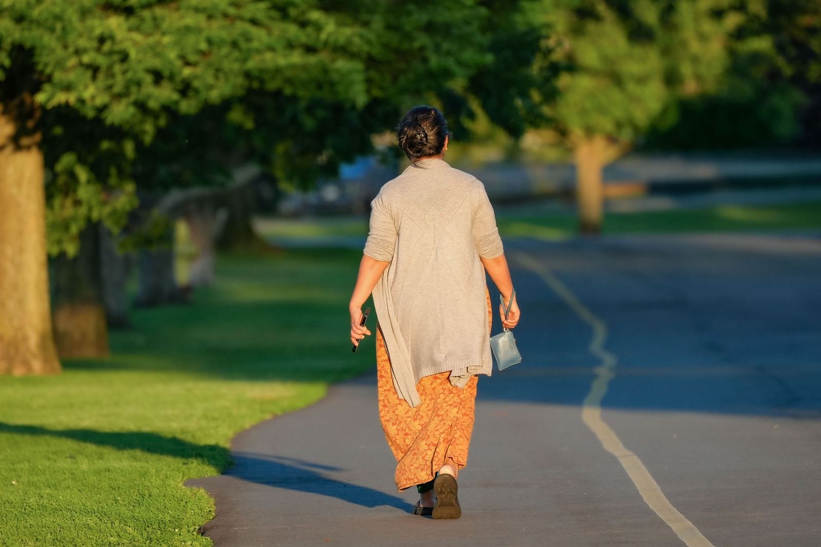 Mujer de espaldas caminando por un sendero arbolado en un parque, con luz cálida de la mañana