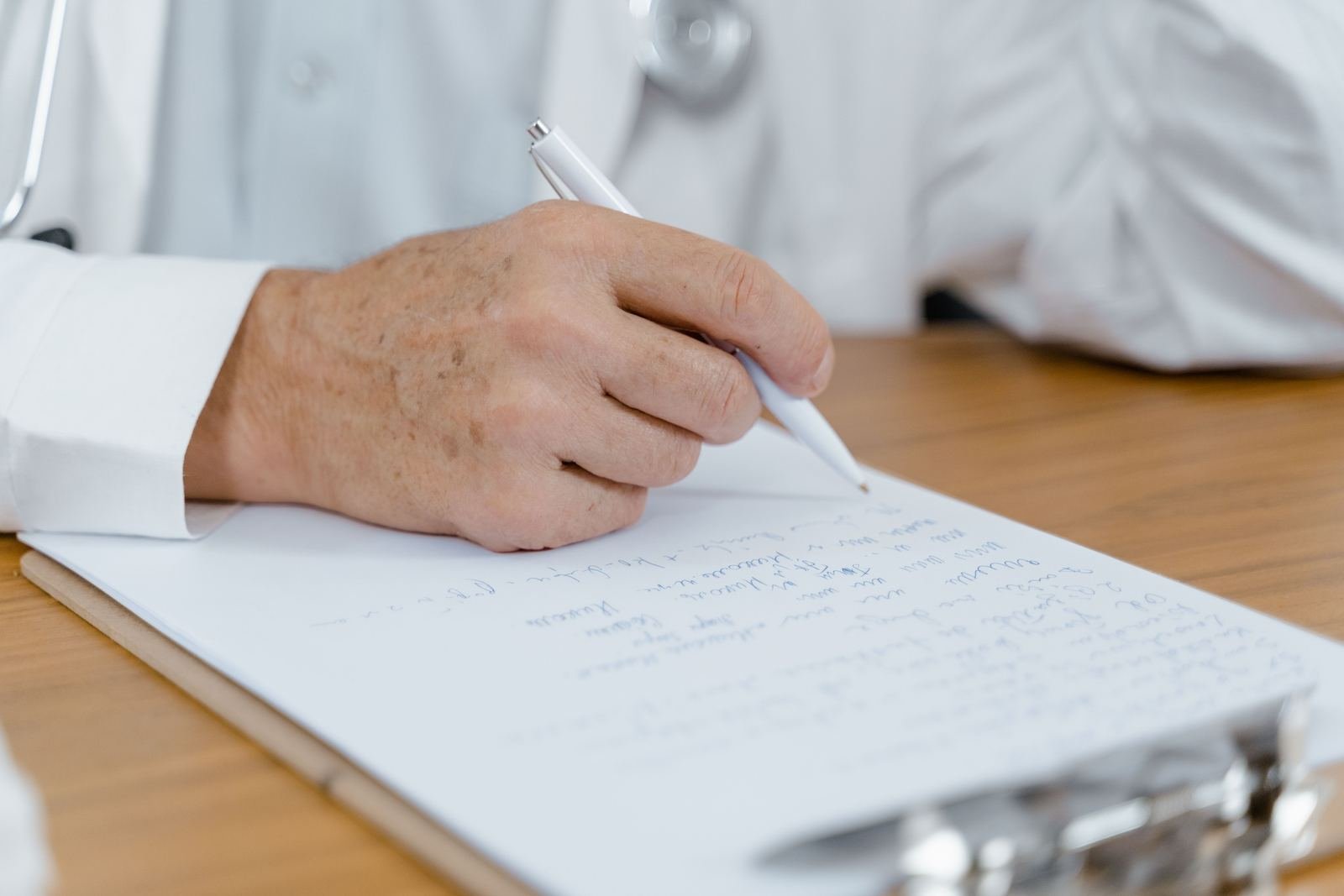 Mano de un médico tomando notas en un formato clínico durante una consulta