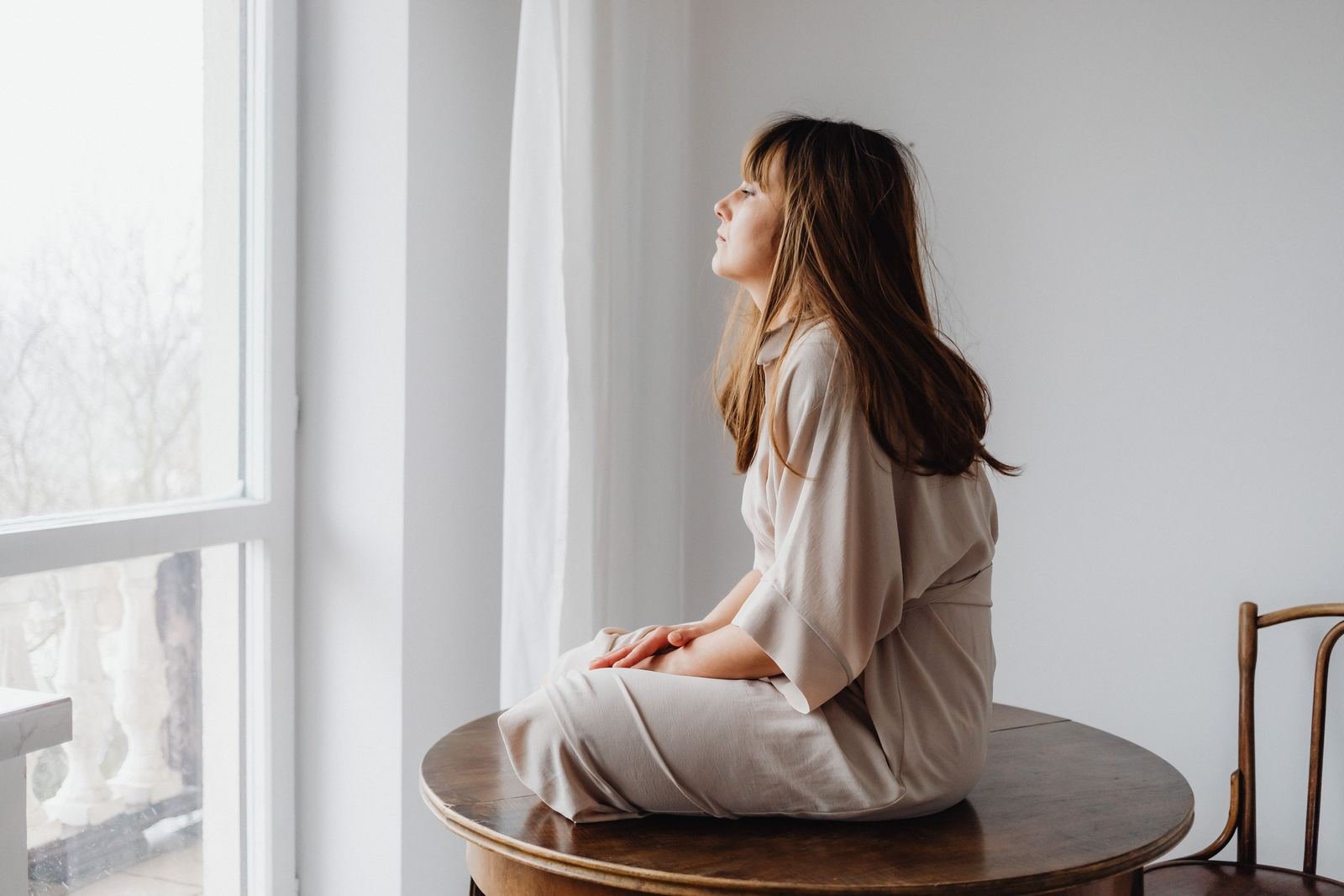 Mujer sentada de perfil junto a una ventana con luz natural, en actitud tranquila