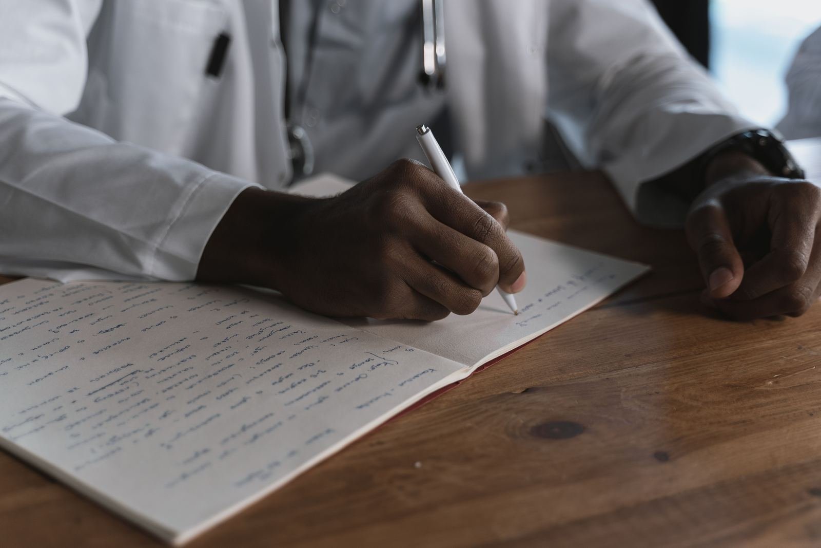 Manos de un doctor escribiendo indicaciones de tratamiento en un consultorio