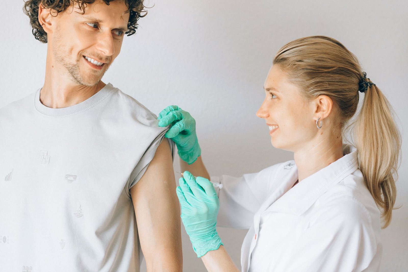 Profesional de la salud, con guantes, aplicando una vacuna en el brazo de un paciente adulto en un consultorio